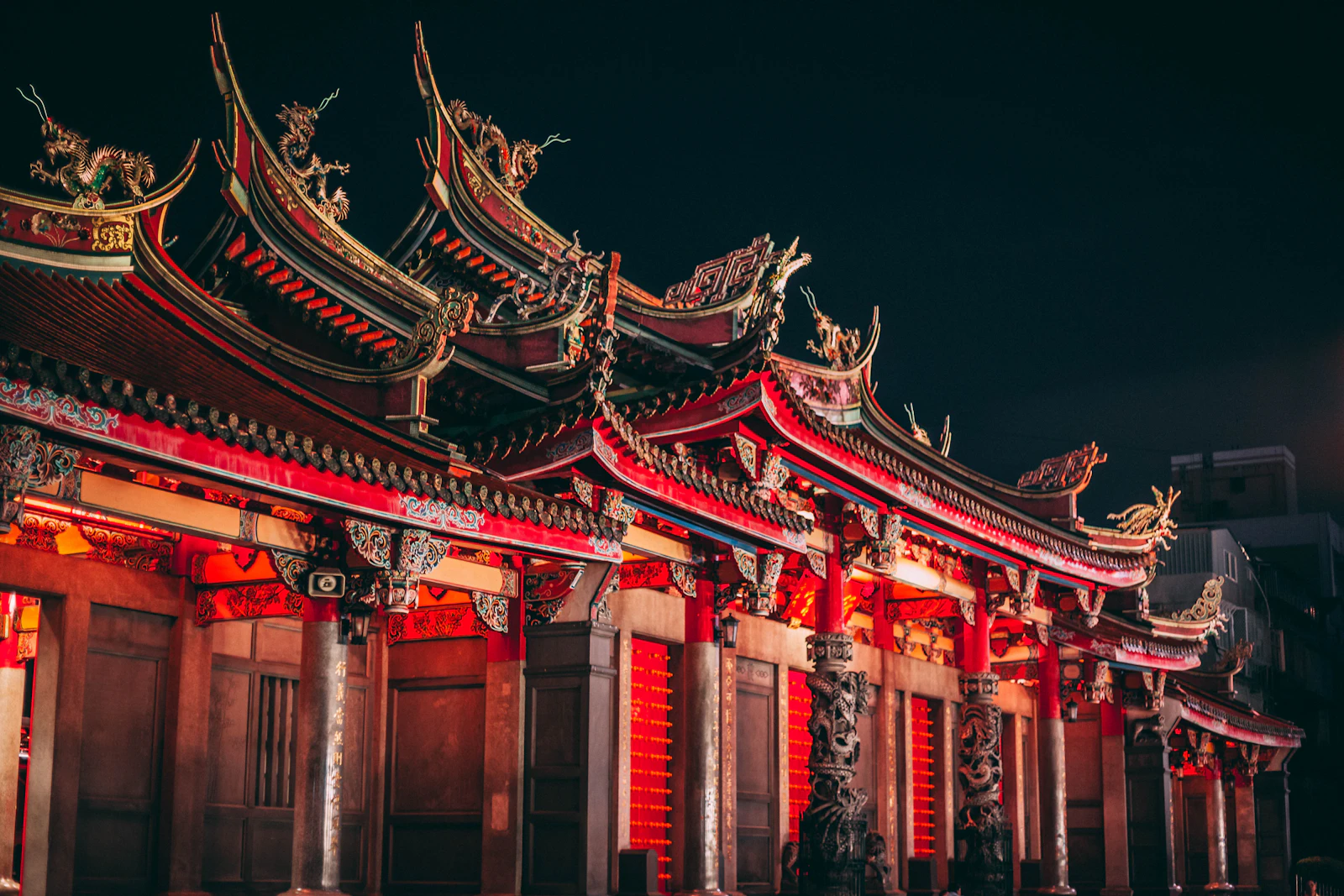 ศาลเจ้าจีนสีแดงประดับไฟยามค่ำคืน หลังคาตกแต่งด้วยรูปปั้นมังกรสีทอง